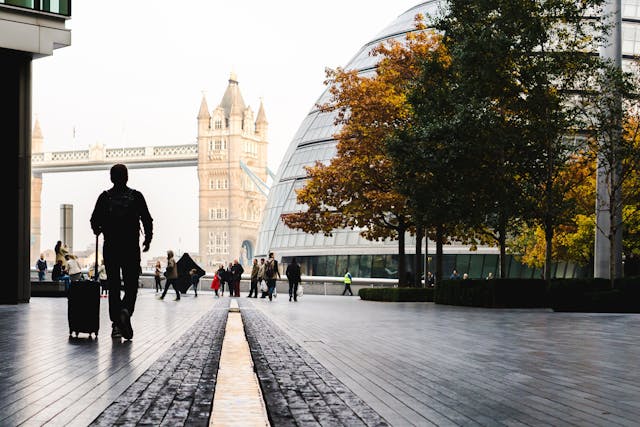 A man is walking away towards London’s Tower Bridge in the distance, pulling along his wheeled suitcase. Image at LondonOfficeSpace.com.