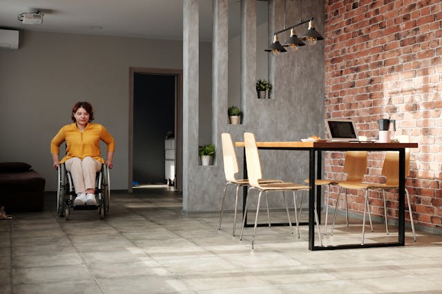A businesswoman in a wheelchair moves down the modern and accessible office break room to her laptop and coffee on the lunch table. Image at LondonOfficeSpace.com.