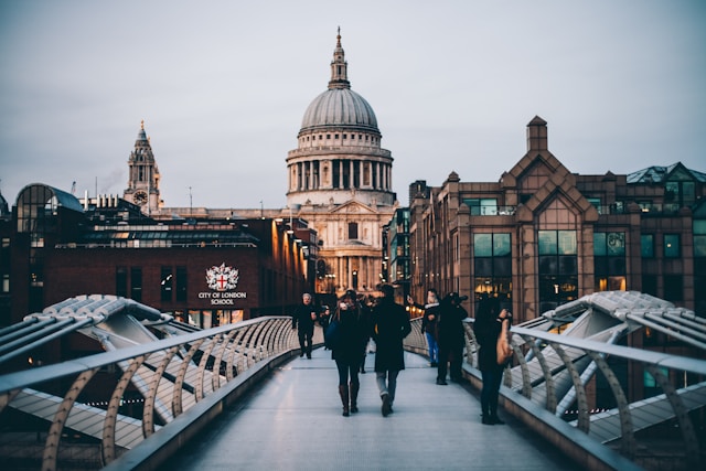 A daytime view along London’s Millennium Bridge towards St Paul’s Cathedral. People are walking on the bridge wearing dark winter clothes, and the cathedral’s dome rises in the distance above buildings on either side. Image at LondonOfficeSpace.com.