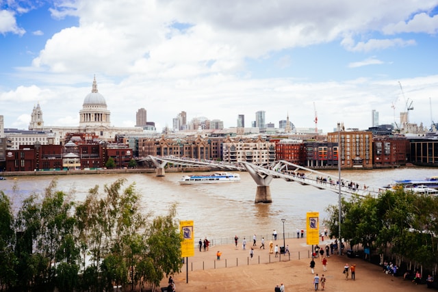 A daytime view down the bank of the River Thames towards the crowded Millennium Bridge and the central London cityscape beyond. Image at LondonOfficeSpace.com.