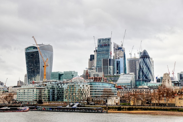 A cloudy, daytime view from the level of the River Thames towards central London’s skyline. There are many building cranes poking up amongst all the iconic skyscrapers. Image at LondonOfficeSpace.com.