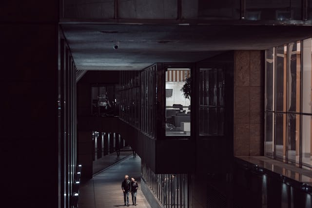 Two men walking together down a faintly lit pathway under and between some modern office buildings in London at night. Image at LondonOfficeSpace.com.